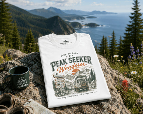 White t-shirt with 'Peak Seeker Wanderer' design on a rock with scenic background