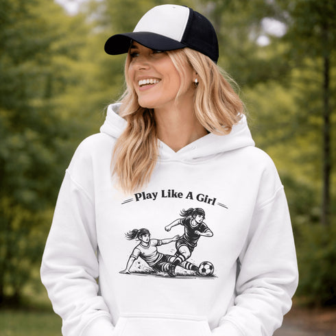 Woman wearing a white Play Like A Girl soccer hoodie with girls soccer graphic, standing on a soccer field with hands in pocket