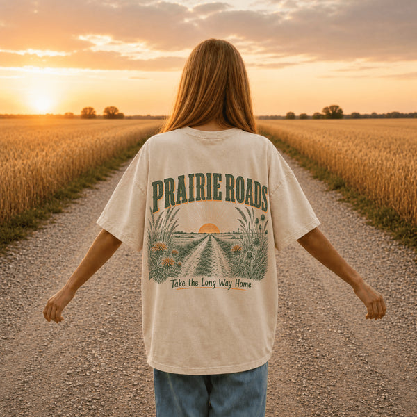Vintage prairie roads graphic on the back of a Comfort Colors t-shirt featuring a gravel road through wheat fields with a prairie sunset and the phrase "Take the Long Way Home."