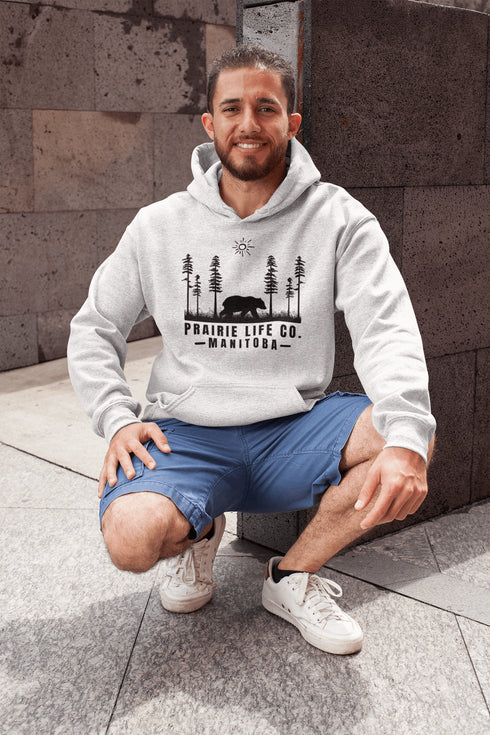 Our Prairie Life Co. Signature Hoodie captures the essence of the wilderness, featuring a striking design of a bear roaming among tall trees.