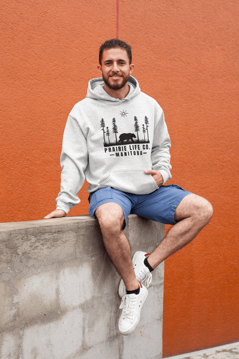 Our Prairie Life Co. Signature Hoodie captures the essence of the wilderness, featuring a striking design of a bear roaming among tall trees.