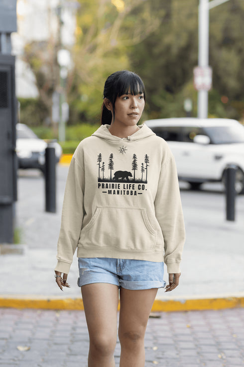 Our Prairie Life Co. Signature Hoodie captures the essence of the wilderness, featuring a striking design of a bear roaming among tall trees.