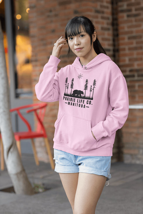 Our Prairie Life Co. Signature Hoodie captures the essence of the wilderness, featuring a striking design of a bear roaming among tall trees.