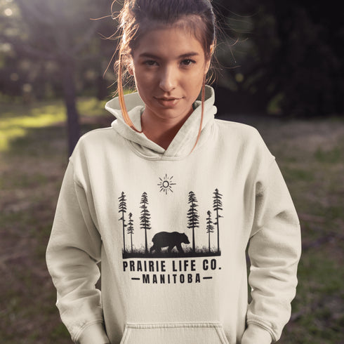 Our Prairie Life Co. Signature Hoodie captures the essence of the wilderness, featuring a striking design of a bear roaming among tall trees.