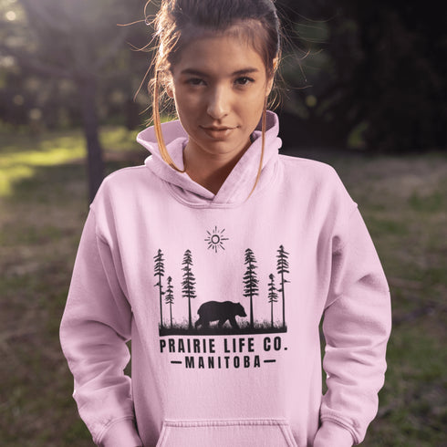 Our Prairie Life Co. Signature Hoodie captures the essence of the wilderness, featuring a striking design of a bear roaming among tall trees.