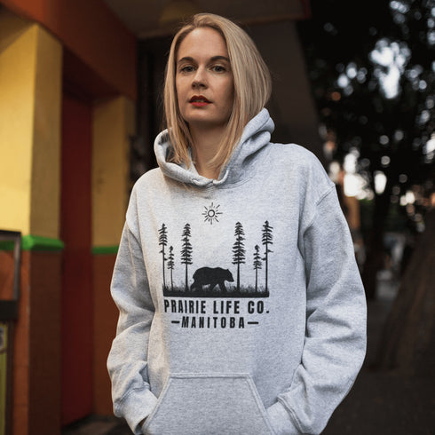 Our Prairie Life Co. Signature Hoodie captures the essence of the wilderness, featuring a striking design of a bear roaming among tall trees.