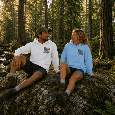 Unisex outdoor hoodie featuring a small coordinating left chest print and large vintage-inspired forest and wildlife graphic on the back, shown in an outdoor lifestyle setting.