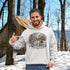 Man wearing a hoodie with a Québec maple syrup cabin design in a snowy outdoor setting.