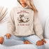 This hoodie features a raccoon—kicked back against a tree stump, wearing a cowboy hat, and looking like it just clocked out of life’s gym membership.