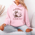 This hoodie features a raccoon—kicked back against a tree stump, wearing a cowboy hat, and looking like it just clocked out of life’s gym membership.