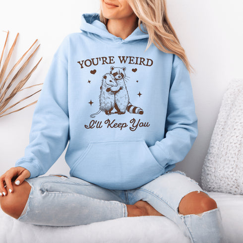 Celebrate the beauty of quirky connections with our comfy hoodie, featuring an adorable illustration of a raccoon and possum sharing a heartwarming hug.