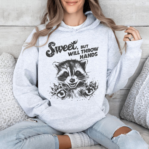Introducing the "Sweet, But Will Throw Hands" Hoodie—perfect for those who are 90% cute and 10% ready to fight (especially over snacks). Featuring a cartoon raccoon that’s equal parts charming and feisty, this hoodie is a gentle reminder that while you're sweet, you’re not to be messed with! 🦝👊