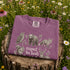 Vintage wildlife graphic on a pepper Comfort Colors t-shirt featuring a bear, fox, owl, squirrel, rabbit, deer, beaver, and lynx with the phrase "Respect the Locals," modeled in a wildflower meadow at sunset.