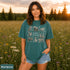 Vintage wildlife graphic on a pepper Comfort Colors t-shirt featuring a bear, fox, owl, squirrel, rabbit, deer, beaver, and lynx with the phrase "Respect the Locals," modeled in a wildflower meadow at sunset.