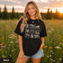Vintage wildlife graphic on a pepper Comfort Colors t-shirt featuring a bear, fox, owl, squirrel, rabbit, deer, beaver, and lynx with the phrase "Respect the Locals," modeled in a wildflower meadow at sunset.