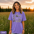 Vintage wildlife graphic on a pepper Comfort Colors t-shirt featuring a bear, fox, owl, squirrel, rabbit, deer, beaver, and lynx with the phrase "Respect the Locals," modeled in a wildflower meadow at sunset.
