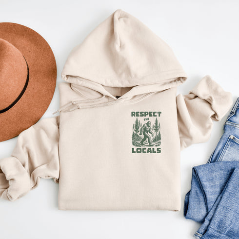 Our Respect the Locals Hoodie features the legend himself—Bigfoot—just casually strolling through the forest like it’s his backyard (because it is).