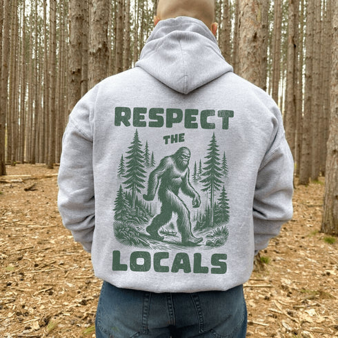Our Respect the Locals Hoodie features the legend himself—Bigfoot—just casually strolling through the forest like it’s his backyard (because it is).