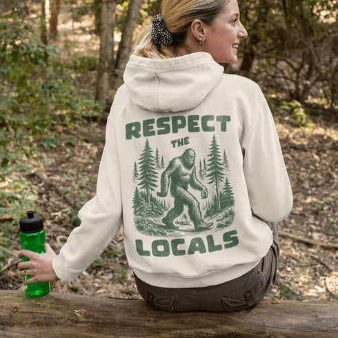 Our Respect the Locals Hoodie features the legend himself—Bigfoot—just casually strolling through the forest like it’s his backyard (because it is).