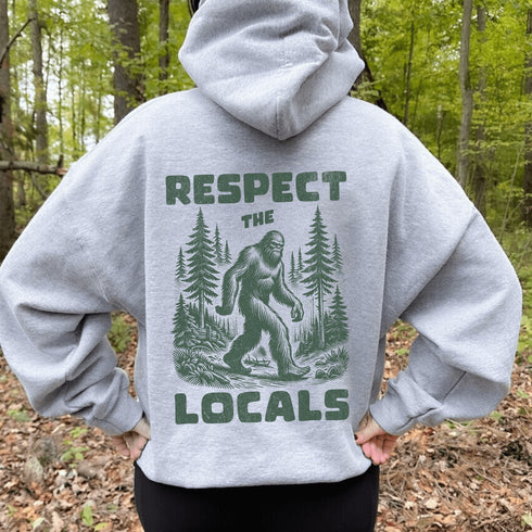 Our Respect the Locals Hoodie features the legend himself—Bigfoot—just casually strolling through the forest like it’s his backyard (because it is).