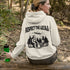 Our Respect the Locals Hoodie features the ultimate forest hangout: Bigfoot and an alien, just two mysterious dudes chilling on logs around a crackling campfire.
