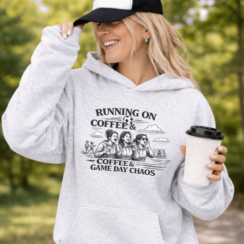 Soccer mom hoodie with “Running on Coffee and Game Day Chaos” design featuring moms cheering on the sidelines with kids playing soccer in the background