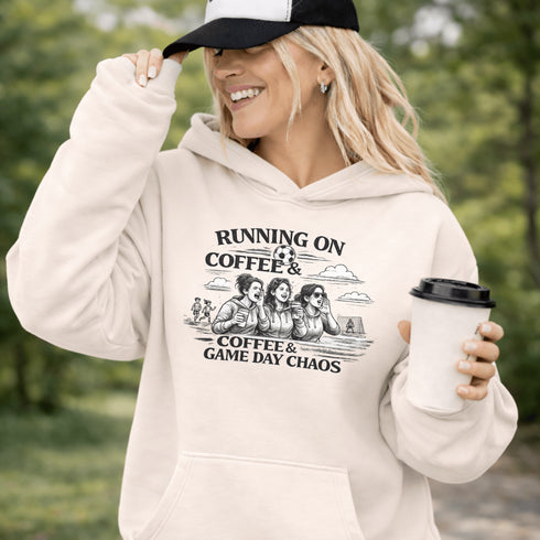 Soccer mom hoodie with “Running on Coffee and Game Day Chaos” design featuring moms cheering on the sidelines with kids playing soccer in the background