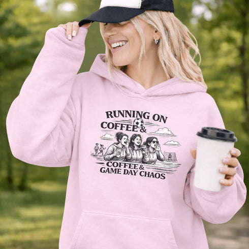 Soccer mom hoodie with “Running on Coffee and Game Day Chaos” design featuring moms cheering on the sidelines with kids playing soccer in the background