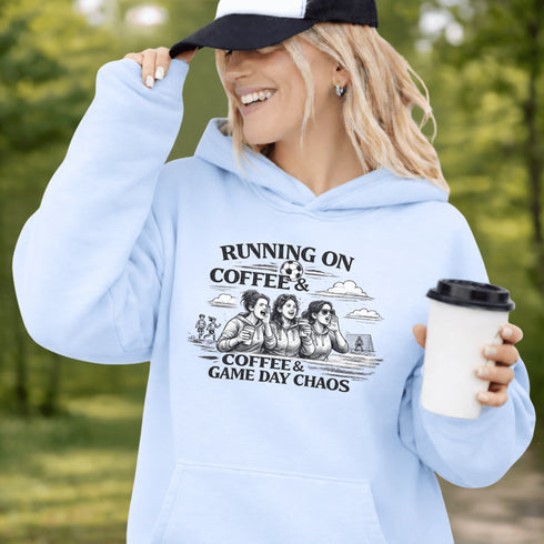 Soccer mom hoodie with “Running on Coffee and Game Day Chaos” design featuring moms cheering on the sidelines with kids playing soccer in the background