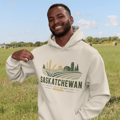 person wearing saskatchewan prairie life hoodie with farm and wheat field design standing in prairie field