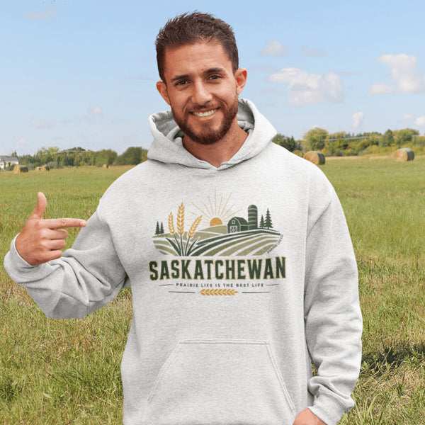 person wearing saskatchewan prairie life hoodie with farm and wheat field design standing in prairie field