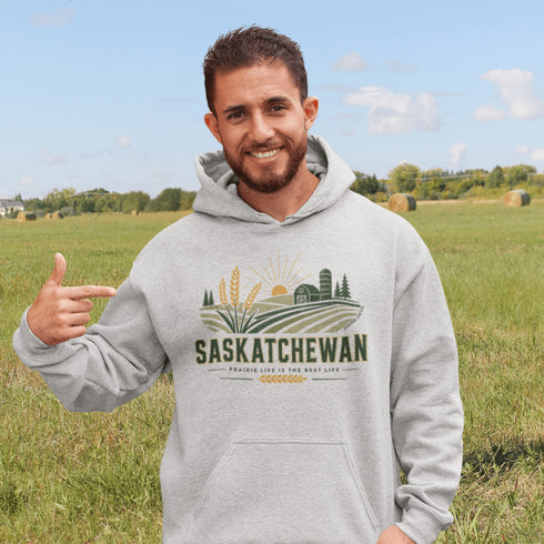 person wearing saskatchewan prairie life hoodie with farm and wheat field design standing in prairie field