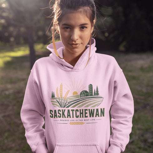person wearing saskatchewan prairie life hoodie with farm and wheat field design standing in prairie field