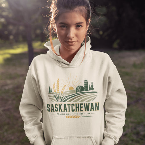 person wearing saskatchewan prairie life hoodie with farm and wheat field design standing in prairie field