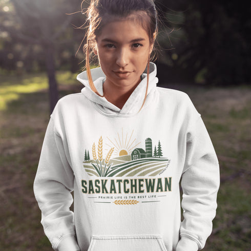 person wearing saskatchewan prairie life hoodie with farm and wheat field design standing in prairie field