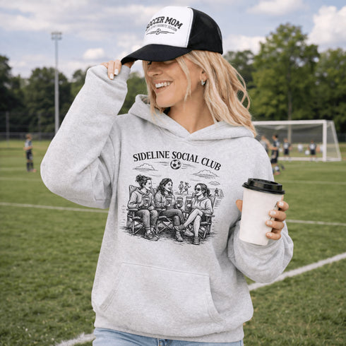Soccer mom hoodie with “Sideline Social Club” design featuring moms sitting in lawn chairs drinking coffee while watching kids play soccer in the background