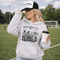 Soccer mom hoodie with “Sideline Social Club” design featuring moms sitting in lawn chairs drinking coffee while watching kids play soccer in the background