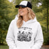 Soccer mom hoodie with “Sideline Social Club” design featuring moms sitting in lawn chairs drinking coffee while watching kids play soccer in the background