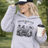 Soccer mom hoodie with “Sideline Social Club” design featuring moms sitting in lawn chairs drinking coffee while watching kids play soccer in the background