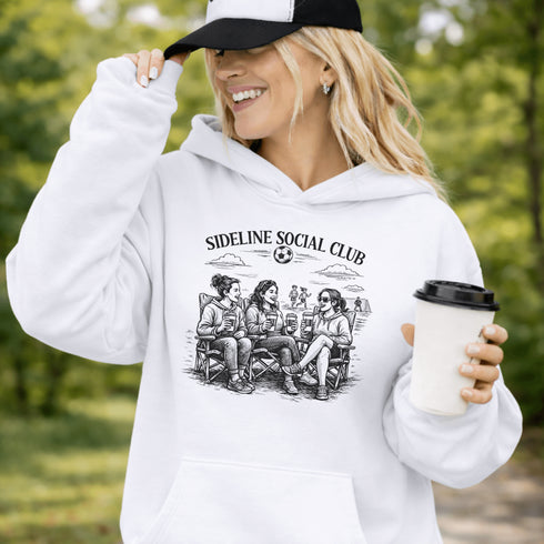 Soccer mom hoodie with “Sideline Social Club” design featuring moms sitting in lawn chairs drinking coffee while watching kids play soccer in the background