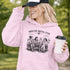 Soccer mom hoodie with “Sideline Social Club” design featuring moms sitting in lawn chairs drinking coffee while watching kids play soccer in the background
