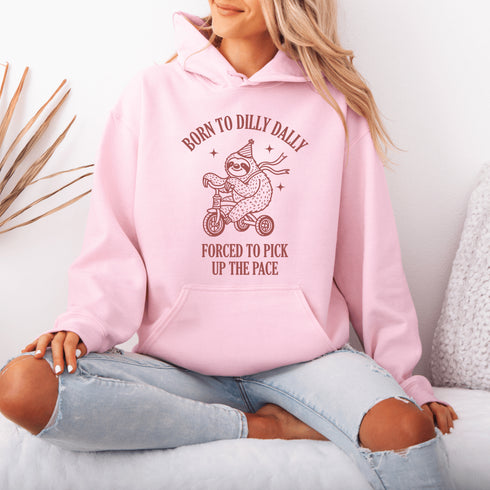 Say hello to the ultimate vibe hoodie: a chill sloth on a tricycle, rocking a party hat and scarf, paired with the painfully relatable words: "Born to dilly dally, forced to pick up the pace."