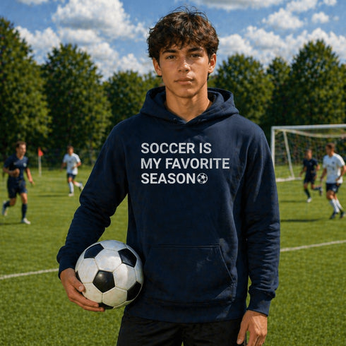Person wearing “Soccer Is My Favorite Season” hoodie holding a soccer ball on a soccer field during a game, casual soccer apparel