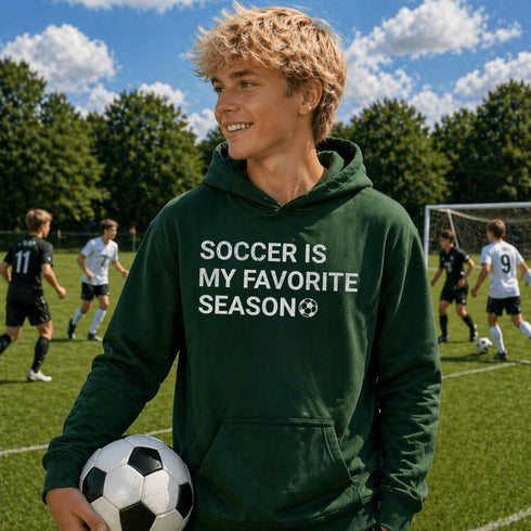 Person wearing “Soccer Is My Favorite Season” hoodie holding a soccer ball on a soccer field during a game, casual soccer apparel
