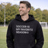 Man wearing a black “Soccer Is My Favorite Season” hoodie on a soccer field during a game, casual soccer apparel