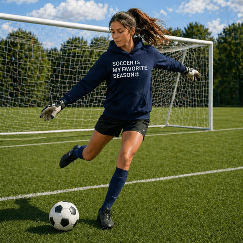 Female Soccer goalie wearing a Navy “Soccer Is My Favorite Season” hoodie kicking a soccer ball during a game, casual soccer apparel