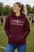 Woman wearing a maroon hoodie with 'Soccer Mom Club' text on a soccer field.