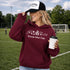 woman wearing soccer mom club hoodie with soccer icons design holding coffee at soccer field