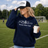 woman wearing soccer mom club hoodie with soccer icons design holding coffee at soccer field