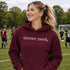 Person wearing “Soccer Nerd” hoodie holding a soccer ball on a soccer field during a game, casual athletic soccer apparel